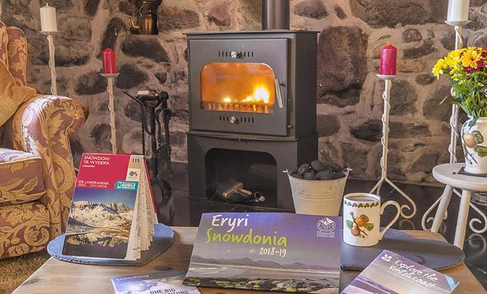 An ingle-nook fire place with candles and a Wood burn stove with a fire lit and a coffe table with some tourist information guides on things to do in